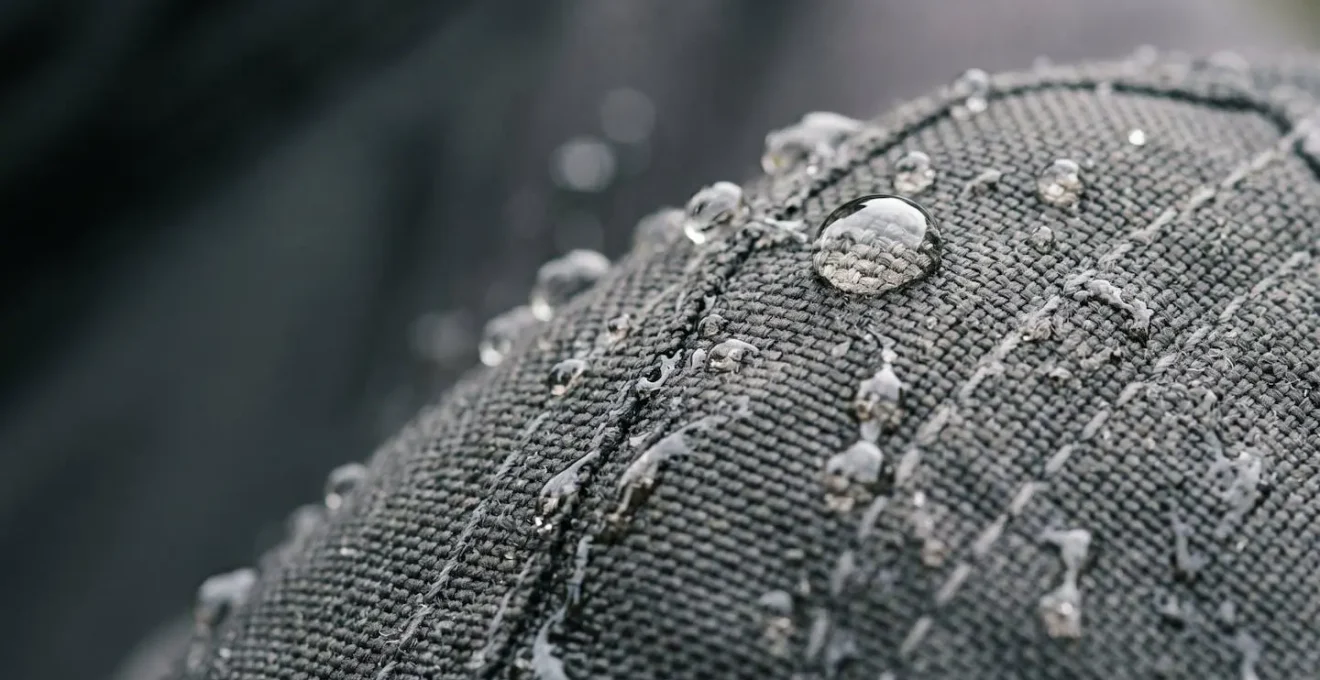 Gros plan sur un blouson de moto textile imperméable avec des gouttes d'eau perlant sur sa surface, illustrant la déperlance et la qualité du traitement hydrofuge